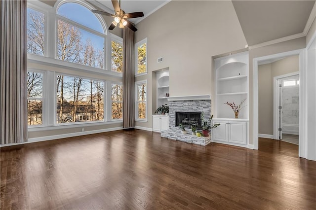 unfurnished living room with dark hardwood / wood-style floors, a high ceiling, built in shelves, ceiling fan, and a stone fireplace