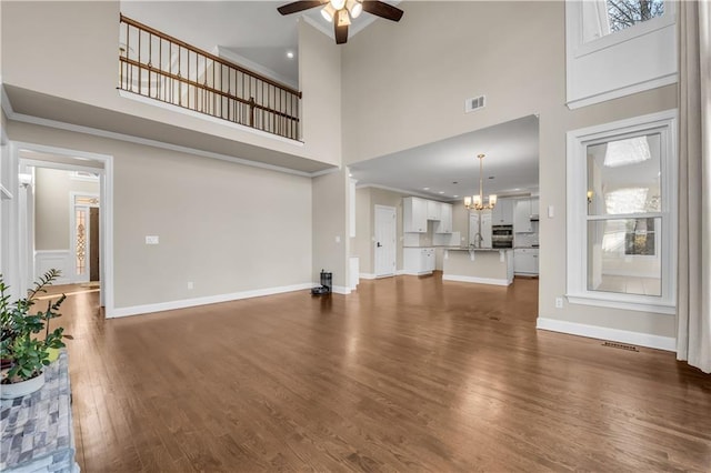 unfurnished living room with a high ceiling, dark wood-type flooring, ceiling fan with notable chandelier, and sink