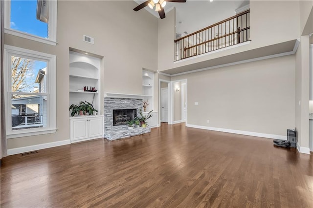 unfurnished living room with a high ceiling, built in shelves, dark hardwood / wood-style flooring, ceiling fan, and a stone fireplace