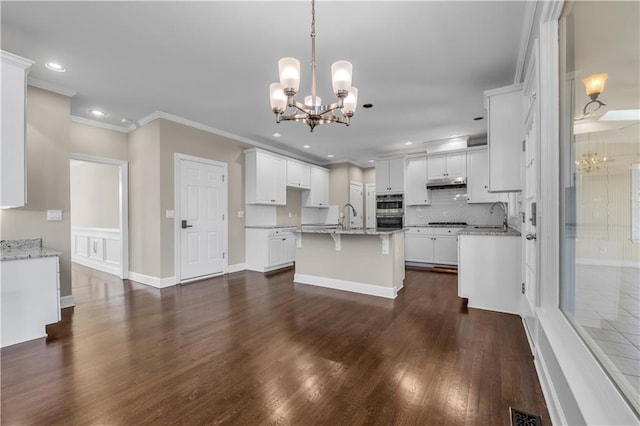 kitchen with a center island with sink, crown molding, a notable chandelier, white cabinets, and decorative light fixtures