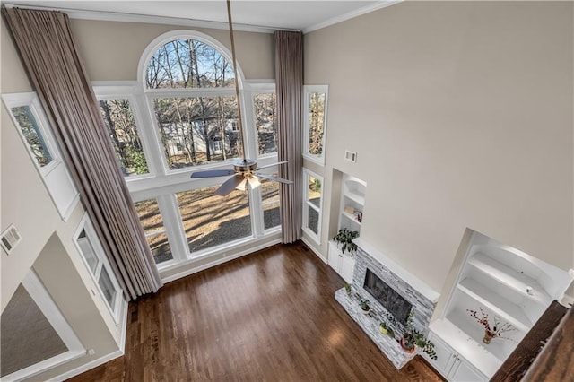 unfurnished living room featuring dark wood-type flooring, ceiling fan, ornamental molding, and a stone fireplace