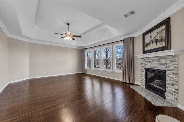 unfurnished living room featuring dark hardwood / wood-style floors, a raised ceiling, ceiling fan, ornamental molding, and a stone fireplace