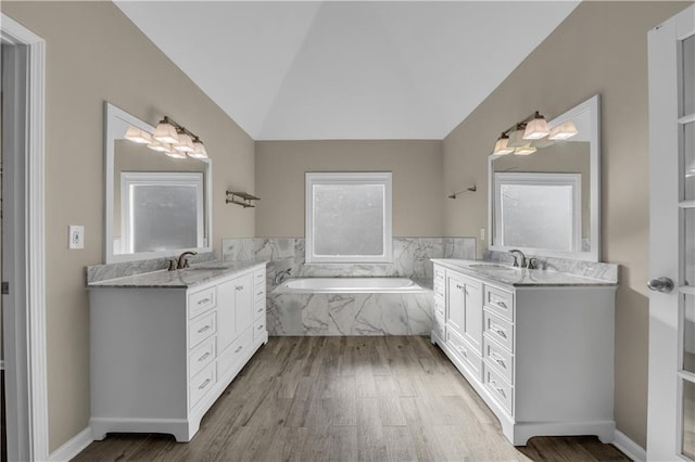 bathroom with hardwood / wood-style floors, tiled tub, lofted ceiling, and vanity