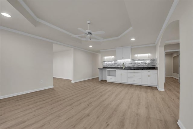 unfurnished living room with light hardwood / wood-style flooring, ceiling fan, a tray ceiling, ornamental molding, and sink