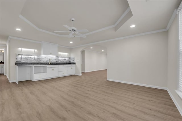 kitchen featuring white cabinets, light hardwood / wood-style floors, decorative backsplash, and a tray ceiling