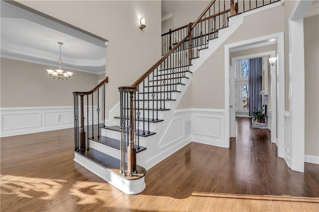 stairway featuring wood-type flooring, an inviting chandelier, a tray ceiling, and crown molding