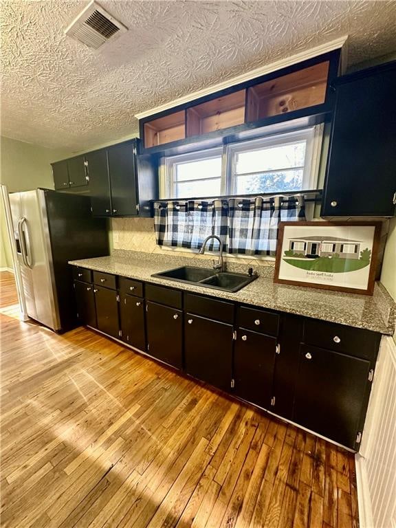 kitchen featuring backsplash, sink, stainless steel refrigerator with ice dispenser, light hardwood / wood-style flooring, and a textured ceiling