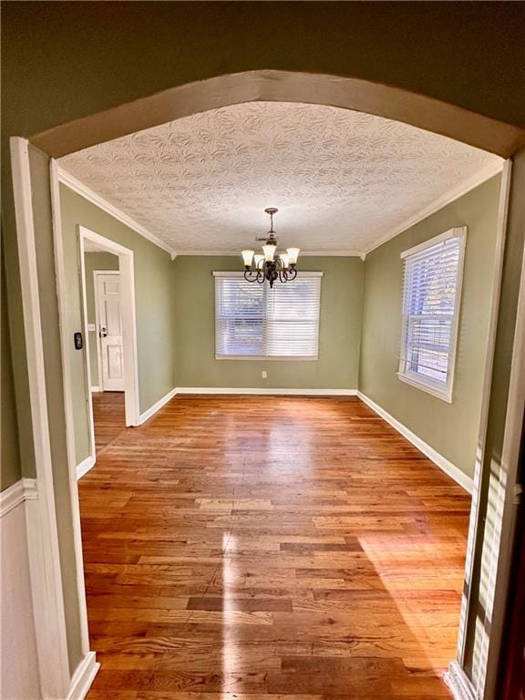 unfurnished dining area with hardwood / wood-style flooring, a healthy amount of sunlight, ornamental molding, and a chandelier