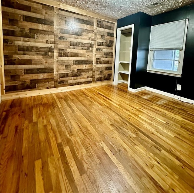 unfurnished room featuring a textured ceiling, light wood-type flooring, and wood walls