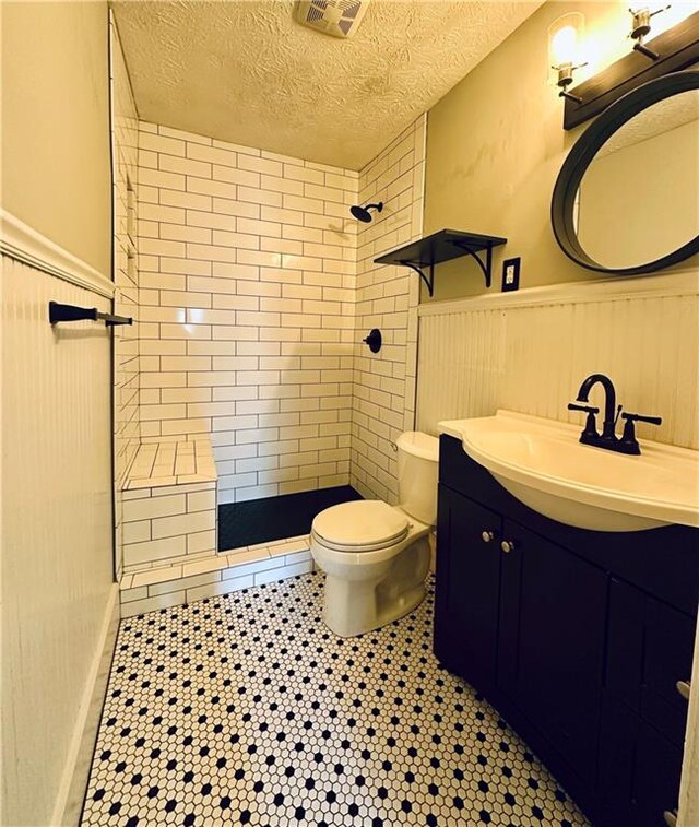 bathroom with tiled shower, vanity, a textured ceiling, and toilet