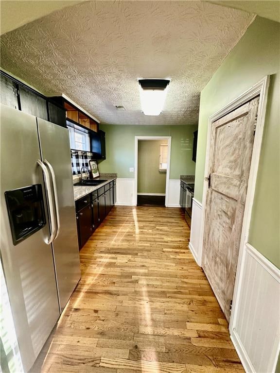 kitchen with dark brown cabinetry, sink, stainless steel fridge with ice dispenser, a textured ceiling, and light wood-type flooring