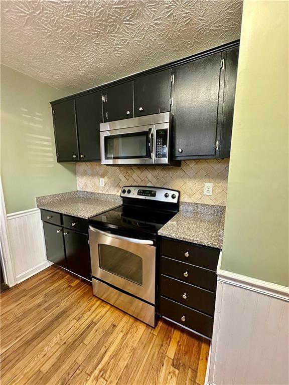 kitchen featuring a textured ceiling, backsplash, appliances with stainless steel finishes, and light hardwood / wood-style flooring