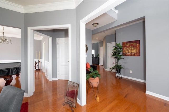 hallway with baseboards, ornamental molding, a chandelier, and wood finished floors