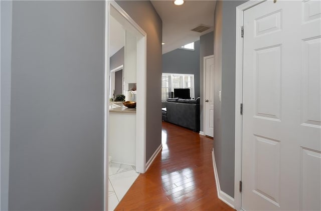 hall with lofted ceiling, wood finished floors, visible vents, and baseboards