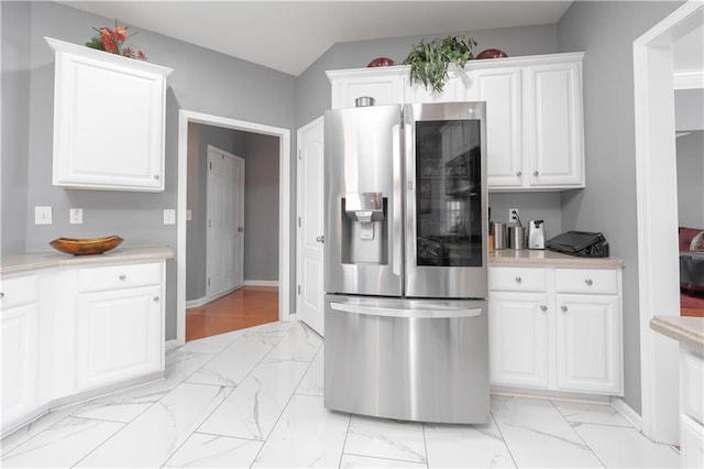 kitchen with marble finish floor, light countertops, stainless steel fridge with ice dispenser, and white cabinets