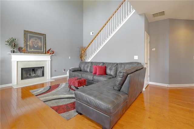 living area with a fireplace with raised hearth, a high ceiling, wood finished floors, visible vents, and baseboards