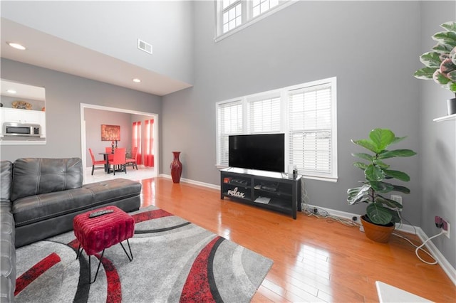 living room with a high ceiling, wood-type flooring, visible vents, and baseboards