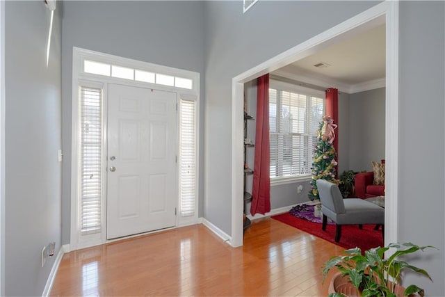 entryway with light wood-style floors, visible vents, ornamental molding, and baseboards