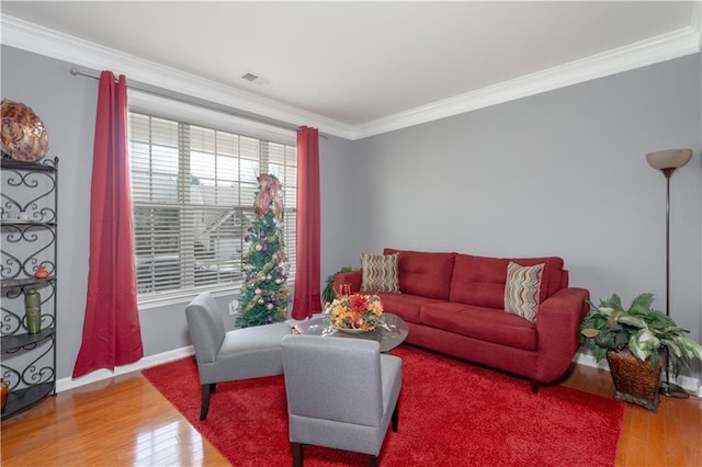 living area with ornamental molding, wood finished floors, visible vents, and baseboards