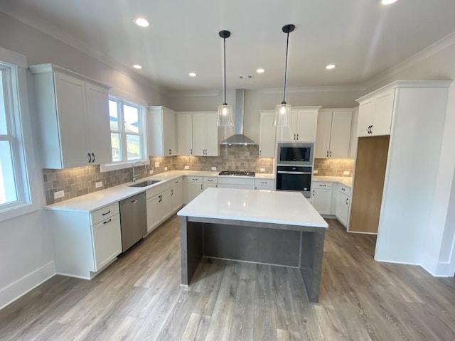 kitchen with wall chimney exhaust hood, a kitchen island, appliances with stainless steel finishes, a sink, and backsplash