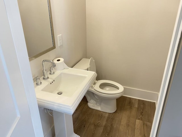 half bath with wood finished floors, toilet, and baseboards