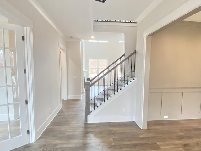 stairs with crown molding, a wainscoted wall, a decorative wall, and wood finished floors