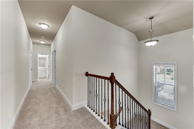 hallway with an upstairs landing, light colored carpet, lofted ceiling, and baseboards