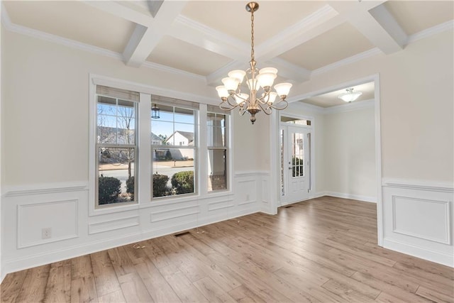 unfurnished dining area with light wood finished floors, plenty of natural light, beamed ceiling, and coffered ceiling