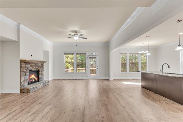 unfurnished living room with a stone fireplace, ceiling fan with notable chandelier, light wood-style floors, and a sink