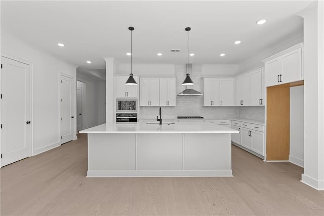 kitchen with white cabinetry, wall chimney range hood, a center island with sink, and black appliances