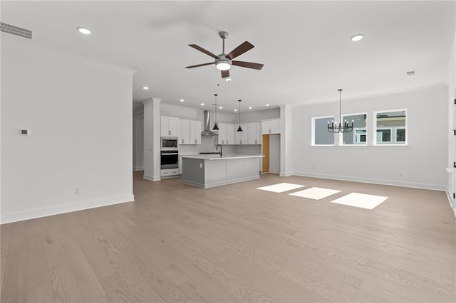 unfurnished living room featuring sink, ceiling fan with notable chandelier, and light wood-type flooring