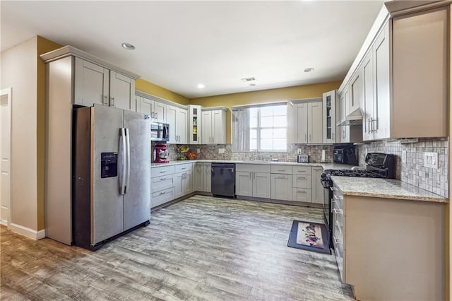 kitchen featuring light wood-style floors, glass insert cabinets, stainless steel appliances, and backsplash