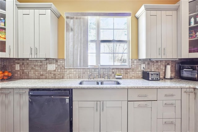 kitchen with tasteful backsplash, dishwasher, a sink, and light stone countertops