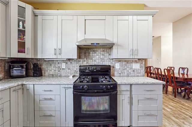 kitchen with decorative backsplash, glass insert cabinets, black range with gas stovetop, light wood-type flooring, and under cabinet range hood