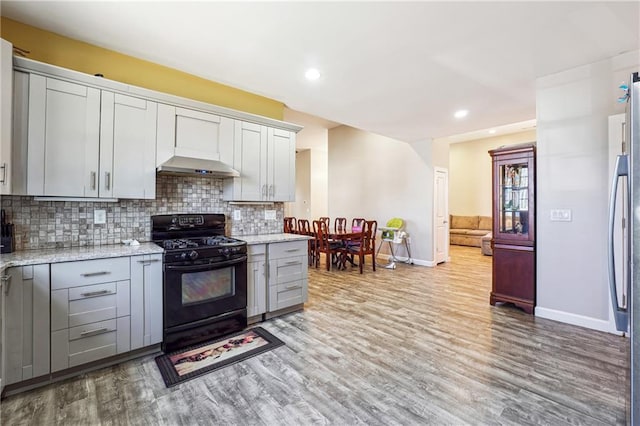 kitchen with light stone counters, light wood finished floors, decorative backsplash, and black range with gas stovetop