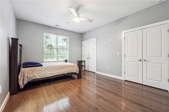 bedroom featuring two closets, visible vents, a ceiling fan, wood finished floors, and baseboards