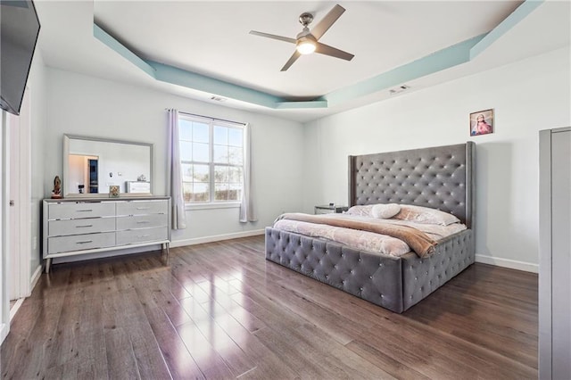 bedroom with a ceiling fan, baseboards, a tray ceiling, and wood finished floors