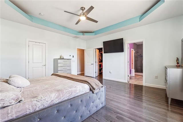 bedroom with wood finished floors, baseboards, a walk in closet, a raised ceiling, and ensuite bath