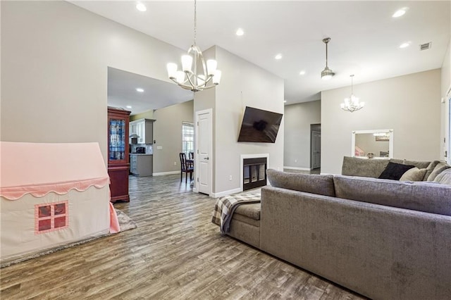 living room featuring an inviting chandelier, recessed lighting, wood finished floors, and a glass covered fireplace