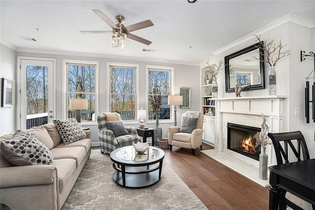 living room featuring ornamental molding, dark wood-style floors, a premium fireplace, a healthy amount of sunlight, and ceiling fan