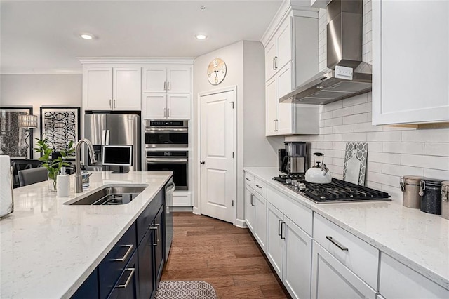 kitchen with wall chimney range hood, appliances with stainless steel finishes, dark wood-style floors, white cabinetry, and a sink