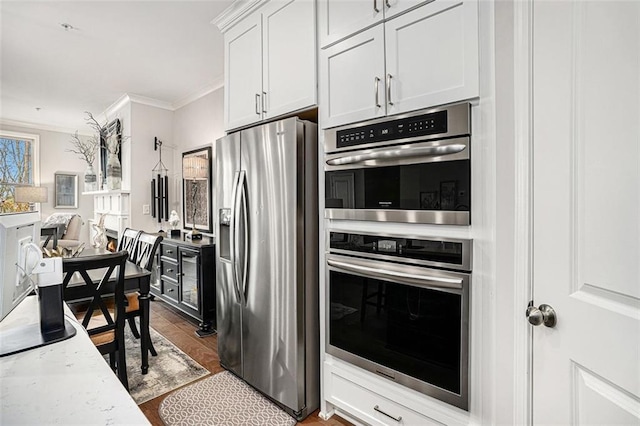 kitchen featuring light stone counters, wood finished floors, ornamental molding, stainless steel appliances, and white cabinetry