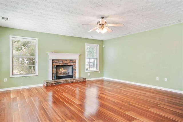 unfurnished living room with ceiling fan, a textured ceiling, a fireplace, and hardwood / wood-style floors