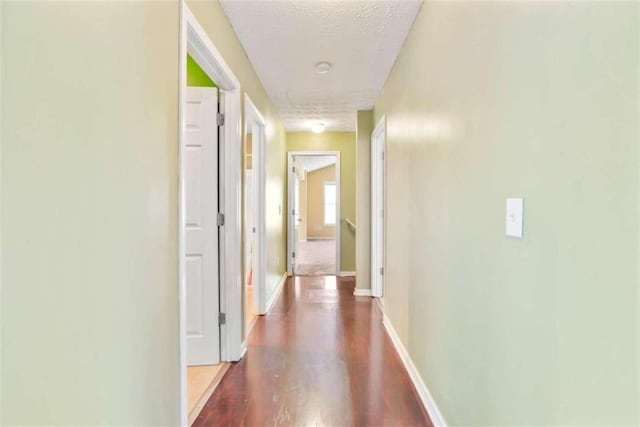 hallway with a textured ceiling and dark hardwood / wood-style flooring