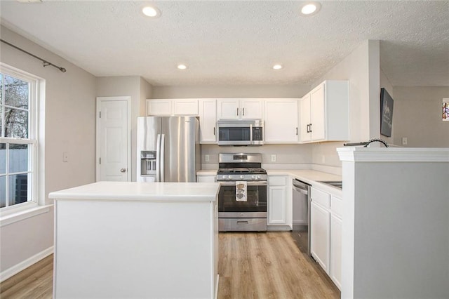 kitchen with light countertops, appliances with stainless steel finishes, a kitchen island, and white cabinetry