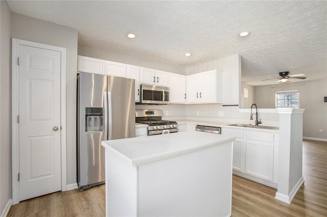 kitchen with white cabinets, a kitchen island, stainless steel appliances, light countertops, and a sink