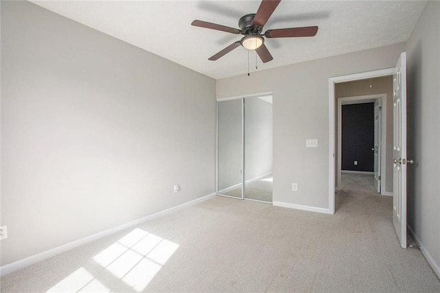 unfurnished bedroom featuring light carpet, a ceiling fan, baseboards, a closet, and attic access