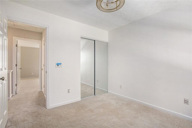 unfurnished bedroom featuring light carpet, a textured ceiling, attic access, and baseboards