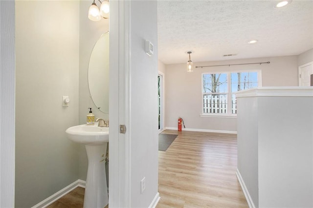 hallway featuring baseboards, a textured ceiling, light wood-style floors, a sink, and recessed lighting