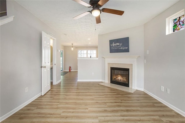 unfurnished living room featuring baseboards, a ceiling fan, a glass covered fireplace, light wood-style flooring, and a textured ceiling